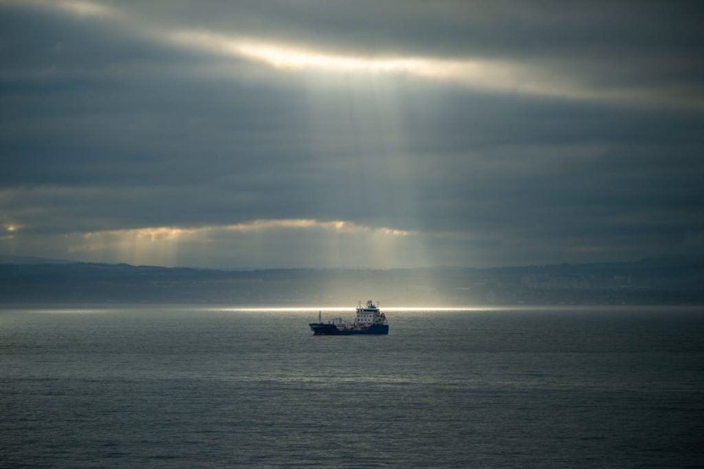 A lone ship on the ocean under dramatic sun rays piercing through clouds, creating a majestic seascape.
